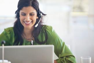 woman wearing headset smiling while looking at a computer