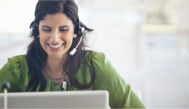 woman smiling while wearing a headset and looking at a computer