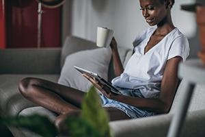 Woman sitting on the couch enjoying a coffee while looking at her electronic bill
